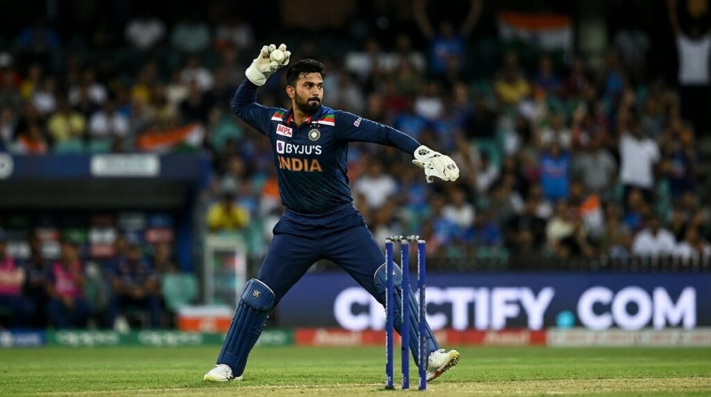 Wicketkeeper in action throwing at stumps with shoulder in overhead position, Crictify.com branding on field advertising